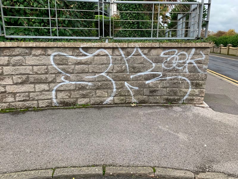 White spray-painted graffiti on a stone block wall before removal