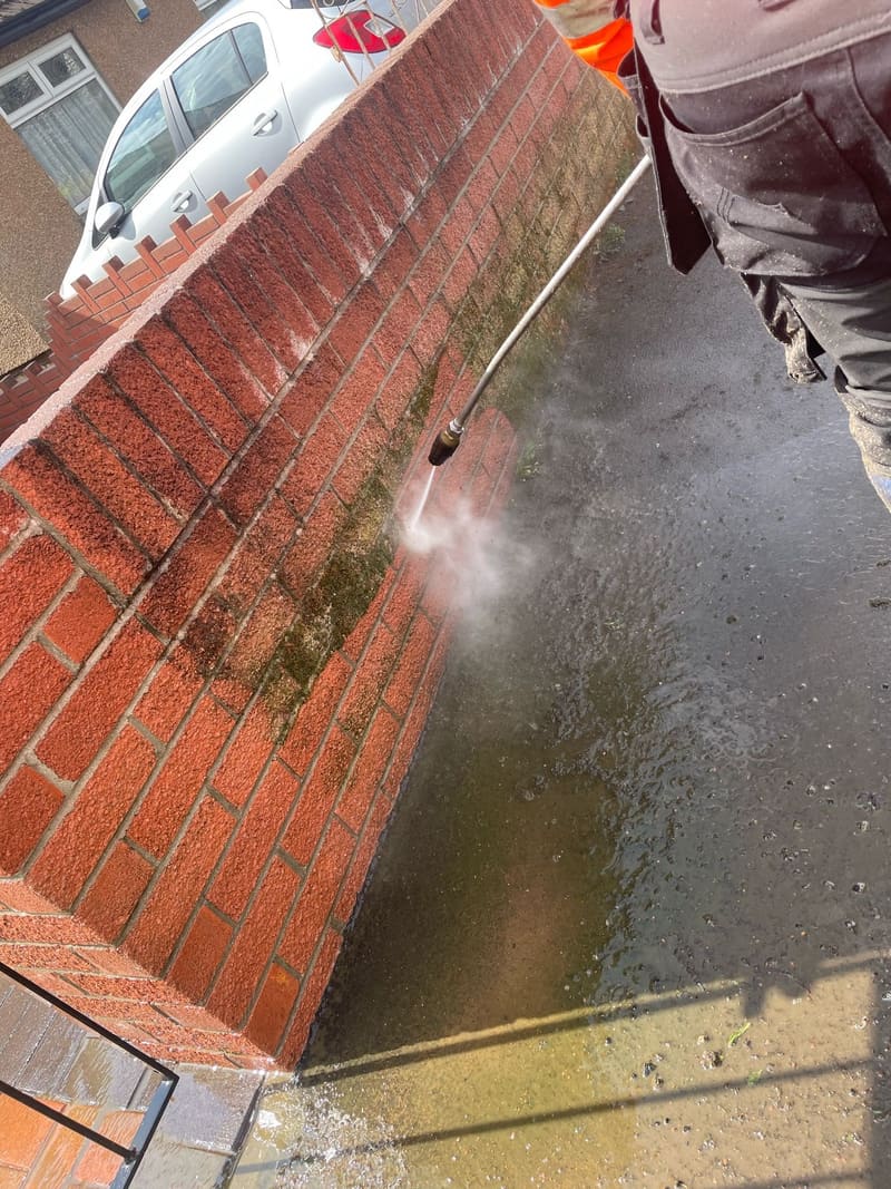 Pressure washing moss off a red brick garden wall