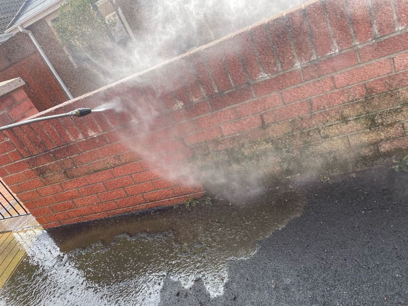 Pressure washing moss and dirt off a red brick wall