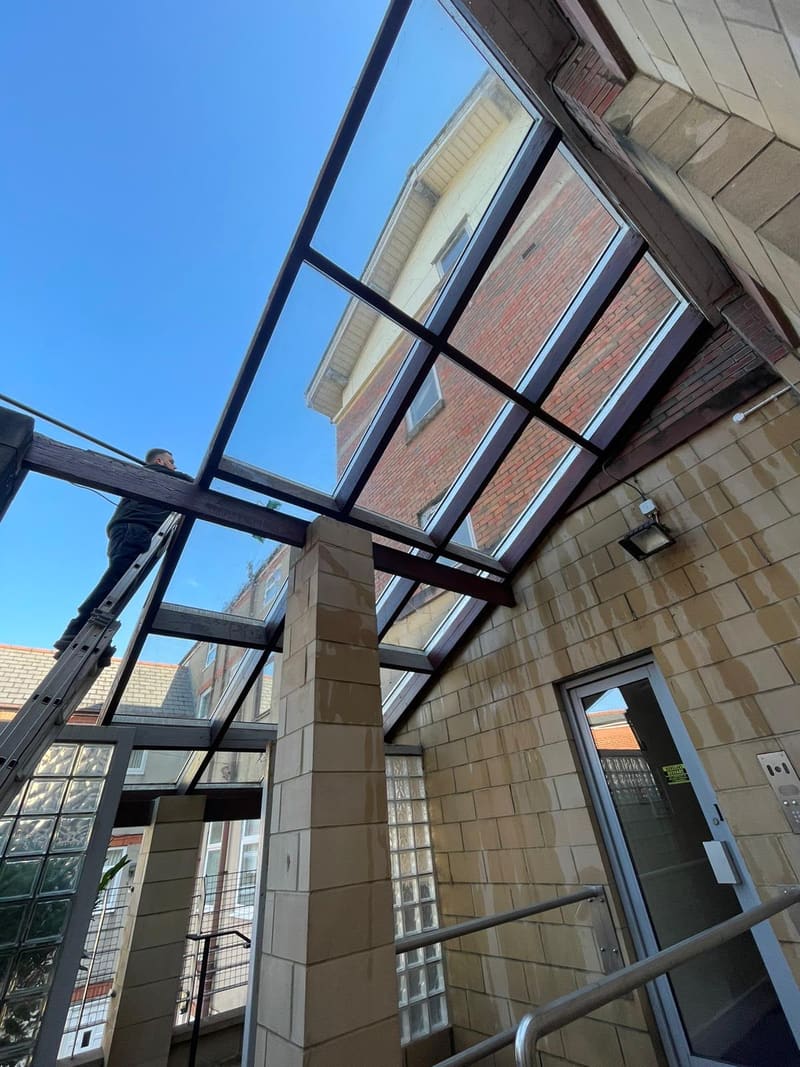 Worker on a ladder cleaning the glass roof canopy of a building