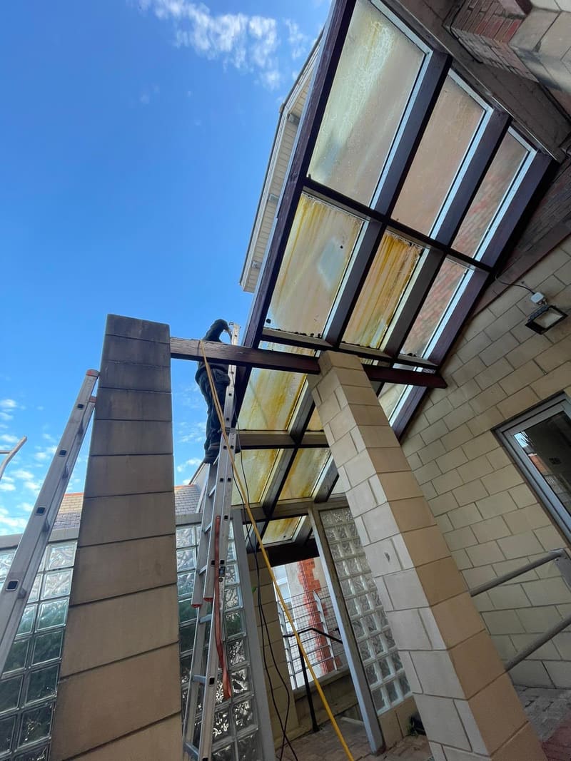 Worker on a ladder cleaning a glass patio canopy