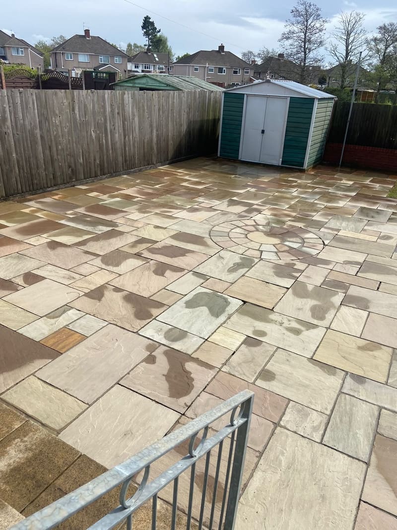 Large sandstone patio with circular design and garden shed