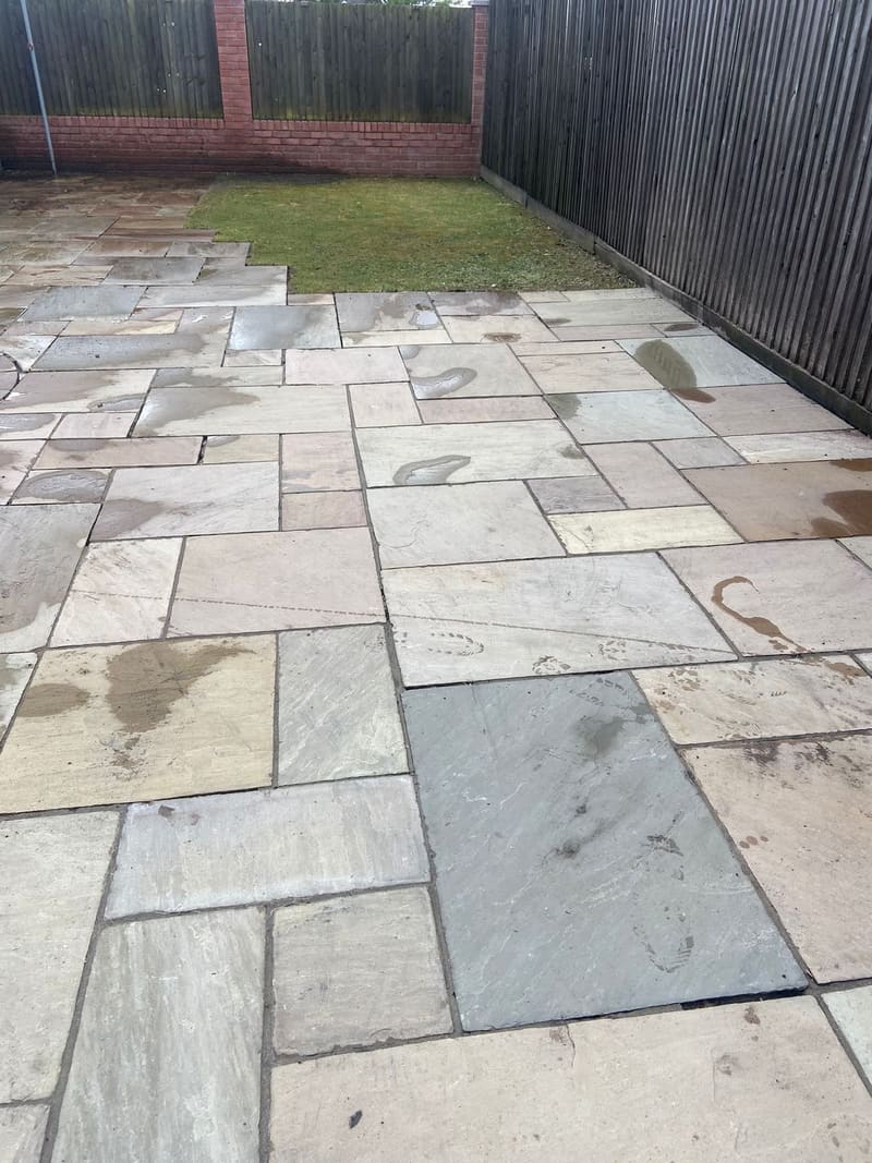 Sandstone patio slabs in a back garden next to a lawn