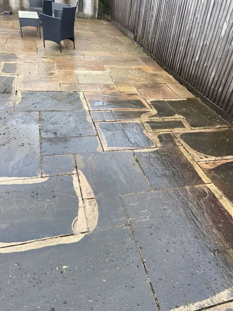 Freshly washed stone patio with garden furniture and fence