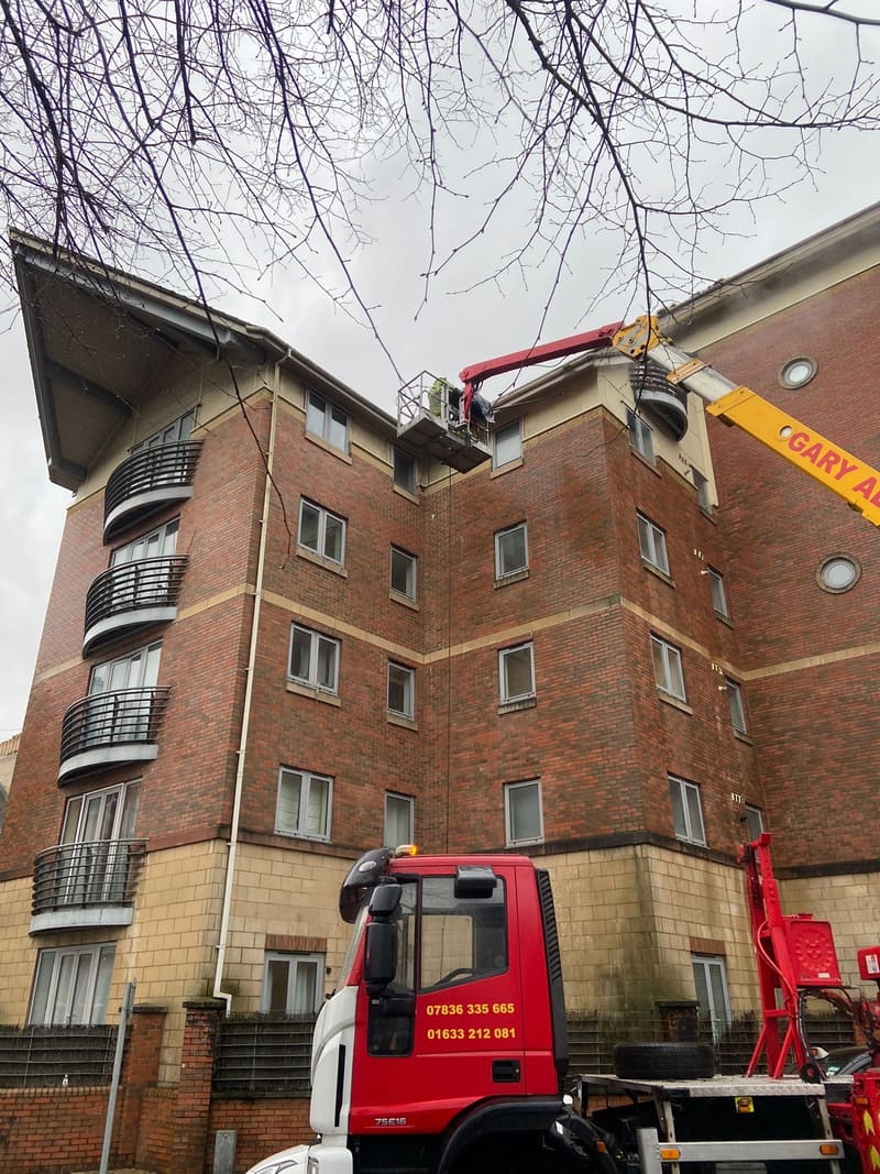 Worker in a cherry picker platform cleaning building gutters