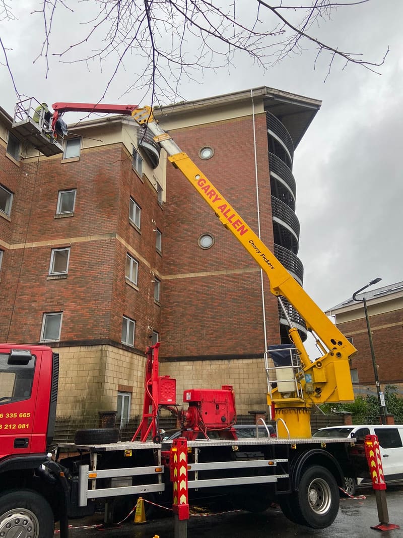 Cherry picker basket at the roofline of a brick building
