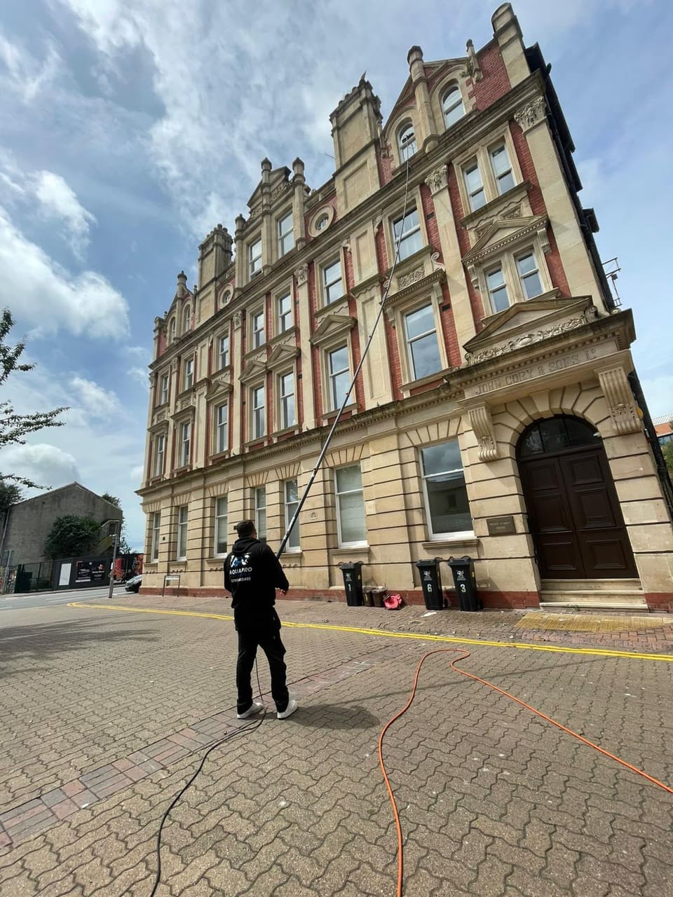 Aqua Pro Cleaning technician using a water-fed pole to clean the windows of a stone building
