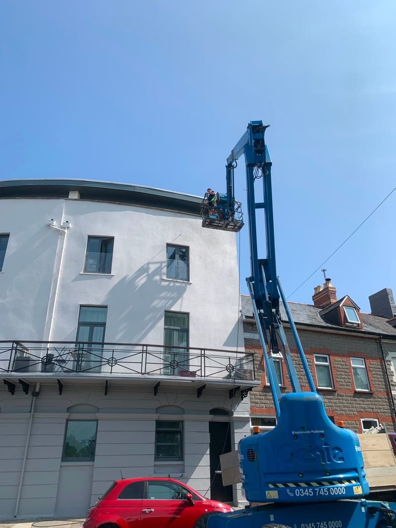 Worker on a cherry picker boom lift beside a white rendered building