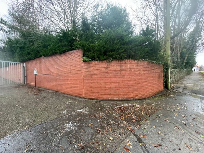 Curved red brick wall topped with evergreen bushes