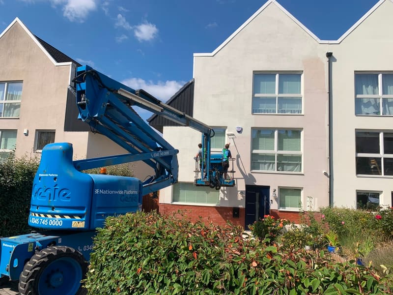 Workers on a cherry picker painting a house facade
