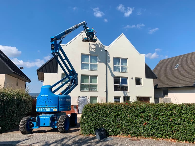 Workers on a cherry picker painting a white house