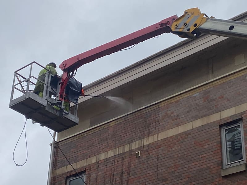 Worker pressure washing a building's fascias from a cherry picker