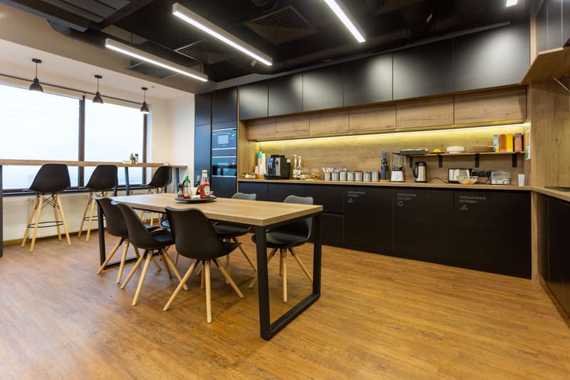 Clean modern office kitchen with wooden table and black chairs